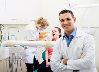 male dentist smiling, dental assistant in background with patient, Guelph, ON affordable dental care